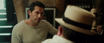 Movie still from “Accident Man: Hitman's Holiday” (2022), directed by George Kirby – A person wearing a hat and looking at a man; Close Up shot, Over the shoulder angle