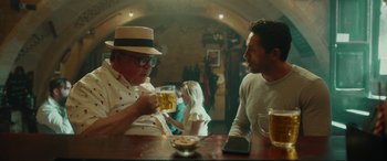 Movie still from “Accident Man: Hitman's Holiday” (2022), directed by George Kirby – Two men are sitting at a table drinking beer; Medium shot, Over the shoulder angle