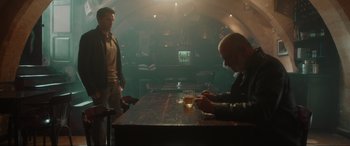 Movie still from “Accident Man: Hitman's Holiday” (2022), directed by George Kirby – Two men are sitting at a table in a bar; Wide shot, Over the shoulder angle