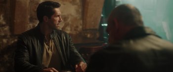 Movie still from “Accident Man: Hitman's Holiday” (2022), directed by George Kirby – A man sitting at a table talking to another man; Medium shot, Over the shoulder angle