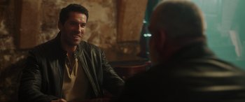 Movie still from “Accident Man: Hitman's Holiday” (2022), directed by George Kirby – A man sitting at a table talking to another man; Medium shot, Over the shoulder angle
