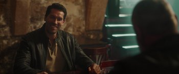 Movie still from “Accident Man: Hitman's Holiday” (2022), directed by George Kirby – A man sitting at a table in a restaurant; Medium shot, Over the shoulder angle