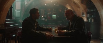 Movie still from “Accident Man: Hitman's Holiday” (2022), directed by George Kirby – Two men sitting at a table in a bar; Medium shot, Over the shoulder angle