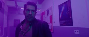 Movie still from “Accident Man: Hitman's Holiday” (2022), directed by George Kirby – A man standing in front of a bulletin board in a purple room; Medium shot, Over the shoulder angle