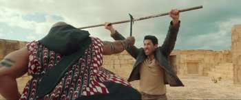 Movie still from “Accident Man: Hitman's Holiday” (2022), directed by George Kirby – A man holding a wooden stick in front of another man; Medium shot, Over the shoulder angle