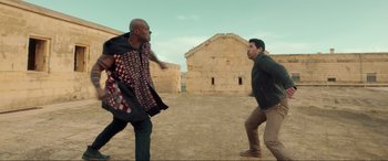 Movie still from “Accident Man: Hitman's Holiday” (2022), directed by George Kirby – Two men are fighting in an open field; Medium shot, Over the shoulder angle