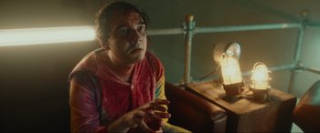 Movie still from “Accident Man: Hitman's Holiday” (2022), directed by George Kirby – A man sitting on a bed holding a banana in his hand; Medium shot, Low angle