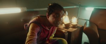 Movie still from “Accident Man: Hitman's Holiday” (2022), directed by George Kirby – A man sitting on the ground in front of some lights; Medium shot, Low angle