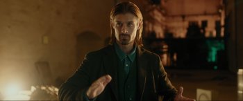 Movie still from “Accident Man: Hitman's Holiday” (2022), directed by George Kirby – A man with long hair wearing a green shirt and a jacket; Close Up shot, Over the shoulder angle