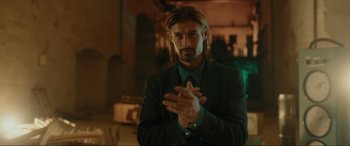 Movie still from “Accident Man: Hitman's Holiday” (2022), directed by George Kirby – A man with long hair clasping his hands; Medium shot, Over the shoulder angle