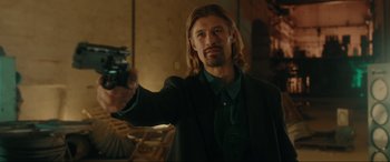 Movie still from “Accident Man: Hitman's Holiday” (2022), directed by George Kirby – A man holding a gun in a room; Medium shot, Over the shoulder angle