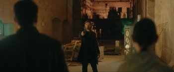 Movie still from “Accident Man: Hitman's Holiday” (2022), directed by George Kirby – A man holding a gun while standing next to a building; Wide shot, Over the shoulder angle