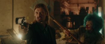 Movie still from “Accident Man: Hitman's Holiday” (2022), directed by George Kirby – A man holding a broom in a room; Medium shot, Over the shoulder angle