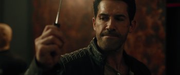 Movie still from “Accident Man: Hitman's Holiday” (2022), directed by George Kirby – A person wearing a leather jacket holding a knife; Close Up shot, Over the shoulder angle