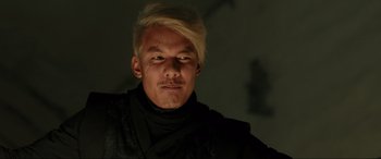 Movie still from “Accident Man: Hitman's Holiday” (2022), directed by George Kirby – A man with blonde hair and a black shirt; Close Up shot, Low angle