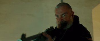 Movie still from “Accident Man: Hitman's Holiday” (2022), directed by George Kirby – A man with a beard holding a gun in a room; Close Up shot, Low angle