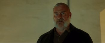 Movie still from “Accident Man: Hitman's Holiday” (2022), directed by George Kirby – An older man with a beard is looking at the camera; Close Up shot, Low angle