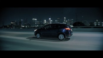 Movie still from “Adverse” (2020), directed by Brian A. Metcalf – A car driving down a street at night with a city skyline in the background; Extreme Wide shot, High angle