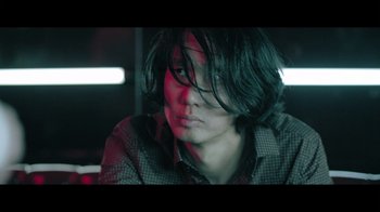 Movie still from “Adverse” (2020), directed by Brian A. Metcalf – A man with long black hair sitting in a dark room; Close Up shot, Low angle