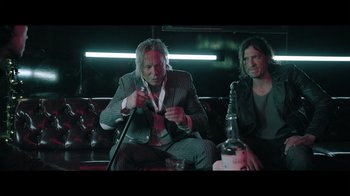 Movie still from “Adverse” (2020), directed by Brian A. Metcalf – Two men are sitting on a couch and one is holding a cell phone; Medium shot, Over the shoulder angle