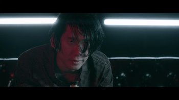 Movie still from “Adverse” (2020), directed by Brian A. Metcalf – A man sitting in a dark room looking at the camera; Close Up shot, Low angle