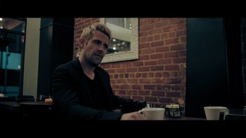 Movie still from “Adverse” (2020), directed by Brian A. Metcalf – A man sitting at a table with a cup of coffee; Medium shot, Over the shoulder angle