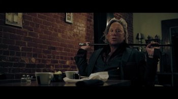 Movie still from “Adverse” (2020), directed by Brian A. Metcalf – A man sitting at a table holding a pipe in his mouth; Medium shot, Low angle