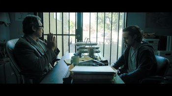 Movie still from “Adverse” (2020), directed by Brian A. Metcalf – Two people sitting at a table with papers on the table; Medium shot, Over the shoulder angle