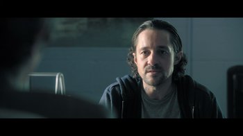 Movie still from “Adverse” (2020), directed by Brian A. Metcalf – A person sitting in a room; Close Up shot, Over the shoulder angle