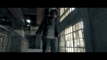 Movie still from “Adverse” (2020), directed by Brian A. Metcalf – A man standing in an abandoned building looking at the camera; Wide shot, Low angle