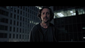 Movie still from “Adverse” (2020), directed by Brian A. Metcalf – A man in a black shirt is standing in front of a building; Close Up shot, Low angle