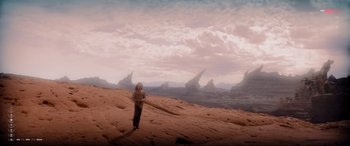 Movie still from “After Earth” (2013), directed by M. Night Shyamalan – A person standing on a sandy beach in front of some mountains; Extreme Wide shot, High angle