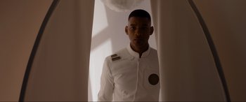 Movie still from “After Earth” (2013), directed by M. Night Shyamalan – A man in a white suit standing in front of a curtain; Medium shot, Low angle