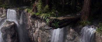 Movie still from “After Earth” (2013), directed by M. Night Shyamalan – A man standing on a fallen tree in front of a waterfall; Extreme Wide shot, High angle