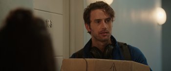 Movie still from “Afterlife of the Party” (2021), directed by Stephen Herek – A man with headphones and a cardboard box in front of him; Close Up shot, Over the shoulder angle
