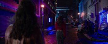 Movie still from “Afterlife of the Party” (2021), directed by Stephen Herek – A woman is standing on the sidewalk at night; Medium shot, Over the shoulder angle