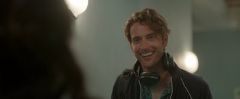 Movie still from “Afterlife of the Party” (2021), directed by Stephen Herek – A man with headphones smiles for the camera; Close Up shot, Over the shoulder angle