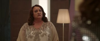 Movie still from “Afterlife of the Party” (2021), directed by Stephen Herek – A woman standing in front of a lamp in a room; Medium shot, Over the shoulder angle