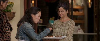 Movie still from “Afterlife of the Party” (2021), directed by Stephen Herek – Two women are holding a plate of pastries; Medium shot, Over the shoulder angle