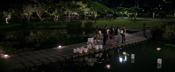 Movie still from “Afterlife of the Party” (2021), directed by Stephen Herek – A group of people standing next to each other near a body of water at night; Extreme Wide shot, High angle