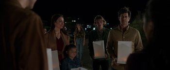 Movie still from “Afterlife of the Party” (2021), directed by Stephen Herek – A group of people standing next to each other holding candles; Medium shot, Over the shoulder angle