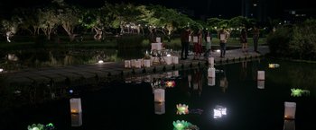 Movie still from “Afterlife of the Party” (2021), directed by Stephen Herek – A group of people standing next to a body of water at night; Extreme Wide shot, High angle