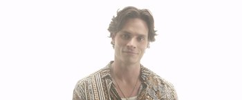 Movie still from “Afterlife of the Party” (2021), directed by Stephen Herek – A man with long brown hair wearing a brown and white shirt; Close Up shot, High angle