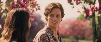 Movie still from “Afterlife of the Party” (2021), directed by Stephen Herek – A man with long brown hair wearing a brown and white patterned shirt; Close Up shot, Over the shoulder angle
