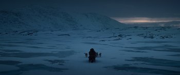 Movie still from “Against the Ice” (2022), directed by Peter Flinth – A man riding a sled down a snow covered slope; Extreme Wide shot, High angle