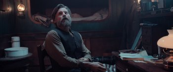 Movie still from “Against the Ice” (2022), directed by Peter Flinth – A man sitting at a desk in front of a computer monitor; Medium shot, Low angle