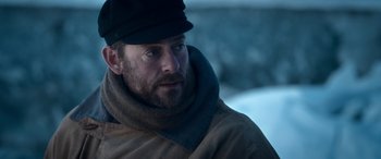 Movie still from “Against the Ice” (2022), directed by Peter Flinth – A man with a beard wearing a hat and a coat; Close Up shot, Low angle