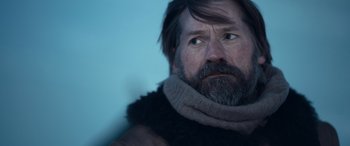 Movie still from “Against the Ice” (2022), directed by Peter Flinth – A man with long hair and a beard wearing a scarf; Close Up shot, Over the shoulder angle