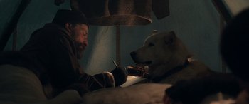 Movie still from “Against the Ice” (2022), directed by Peter Flinth – A man and a white dog sitting next to each other on a bed; Medium shot, High angle