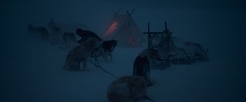 Movie still from “Against the Ice” (2022), directed by Peter Flinth – A group of dogs standing in the snow next to a tent; Wide shot, High angle